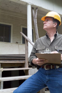 Contractor wearing hardhat and writing on clipboard outside of home improvement project.