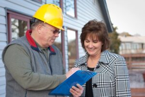 Contractor wearing hardhat showing clipboard to female homeowner.