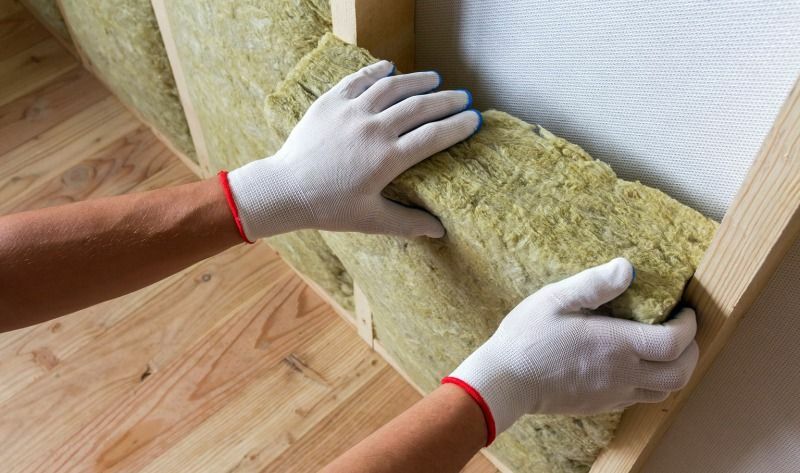 Gloved hands installing mineral wool insulation in an interior wall.