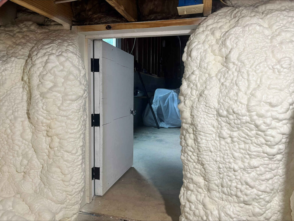 Access door as viewed from inside a conditioned crawl space featuring vapor barrier and 3.5" of open cell spray foam applied to foundation walls.