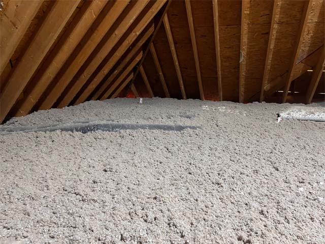 Blown-in cellulose insulation covering the floor of a residential attic with exposed wooden rafters, installed by Toler Insulating
