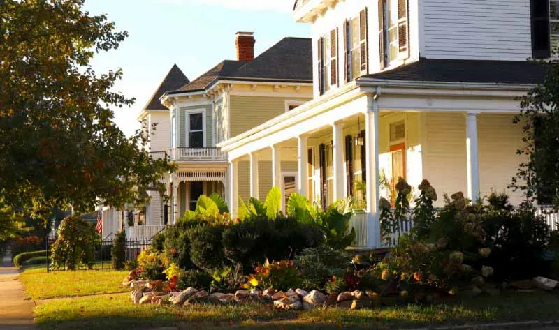 Row of historic homes with wraparound porches and landscaped gardens in warm evening light, representing energy-efficient upgrades for residential insulation.