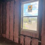 Pink fiberglass batt insulation installed around a window frame during a Toler Insulating retrofit project for improved energy efficiency.