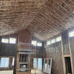 Unfaced fiberglass batt insulation installed in cathedral ceiling rafters and wall cavities of a large new construction home with scaffolding and clerestory windows.