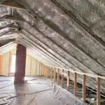Toler Insulating closed cell spray foam sealing the roof deck along the full attic roofline around a brick chimney in Lynchburg, VA.